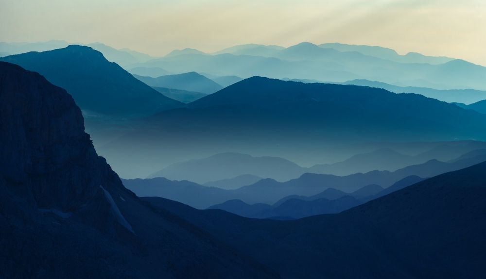 Layers of mountains with a blue hue silhouetted against a setting sun. Emphasis on the mountains to discuss gifts for outdoorsy women.