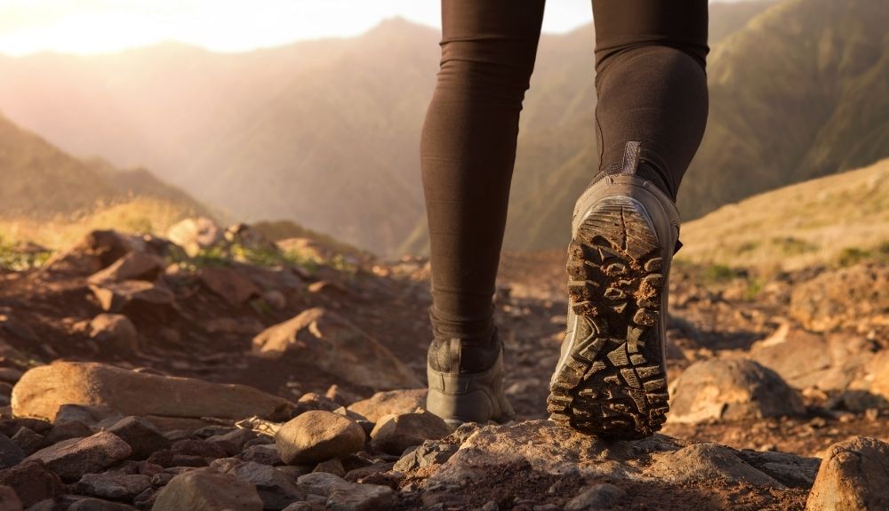Mountains in the background, with tough terrain and muddy hiking boots in the foreground showcasing one of the great gifts for outdoorsy women.
