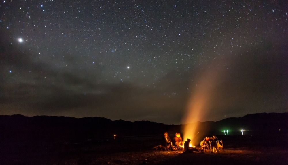 Night sky with people gathered around a campfire. This picture highlights camping gear gifts for outdoorsy women.