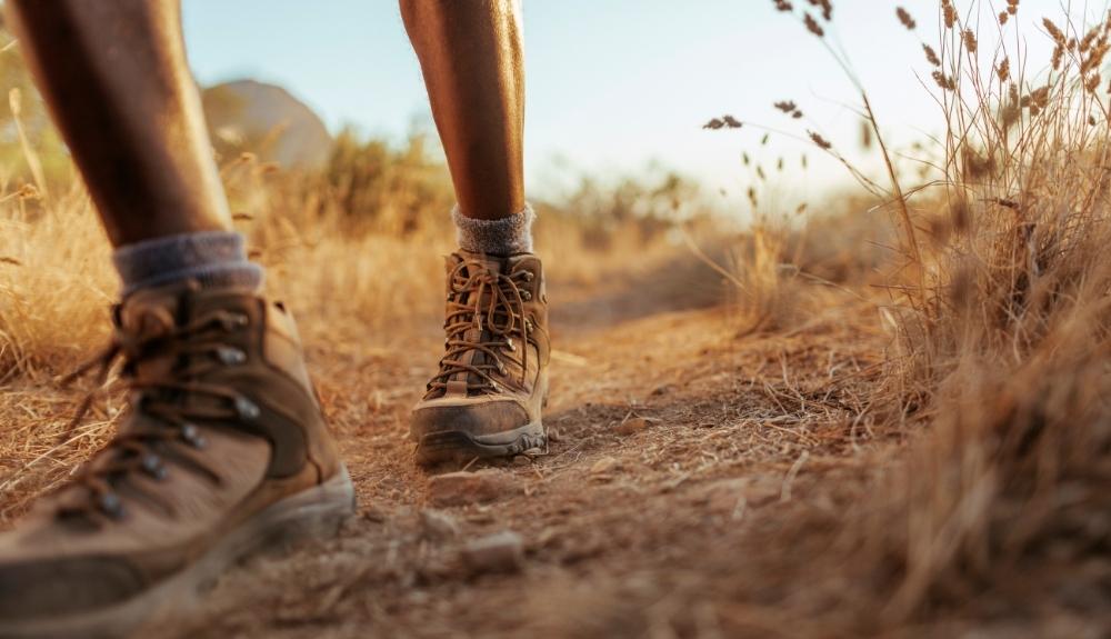 Hiking boots and lower legs in the foreground of grassy terrain. Picture used for emphasis on Gadgets for Hikers information.