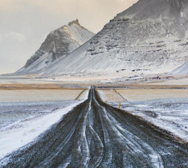 Road down the center of the photo, mountains in the background, everything is covered in snow. Picture of Iceland to emphasize Books about Iceland.