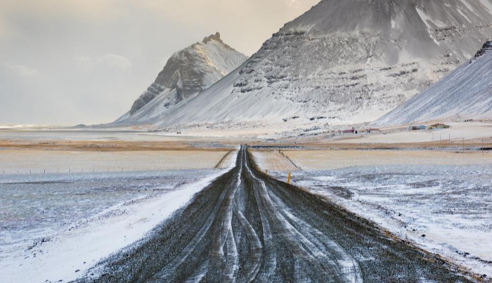 Road down the center of the photo, mountains in the background, everything is covered in snow. Picture of Iceland to emphasize Books about Iceland.