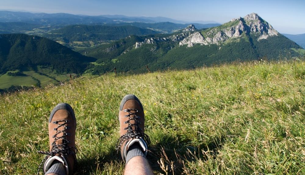 Two feet in hiking boots in the foreground, a view of mountains and greenery in the background. Emphasis on books for hikers.