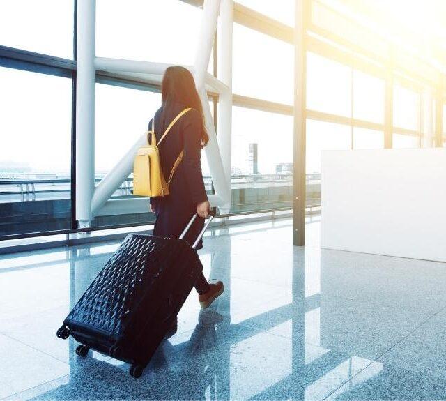 Woman dragging suitcase through airport terminal, emphasis on travel essentials for women.
