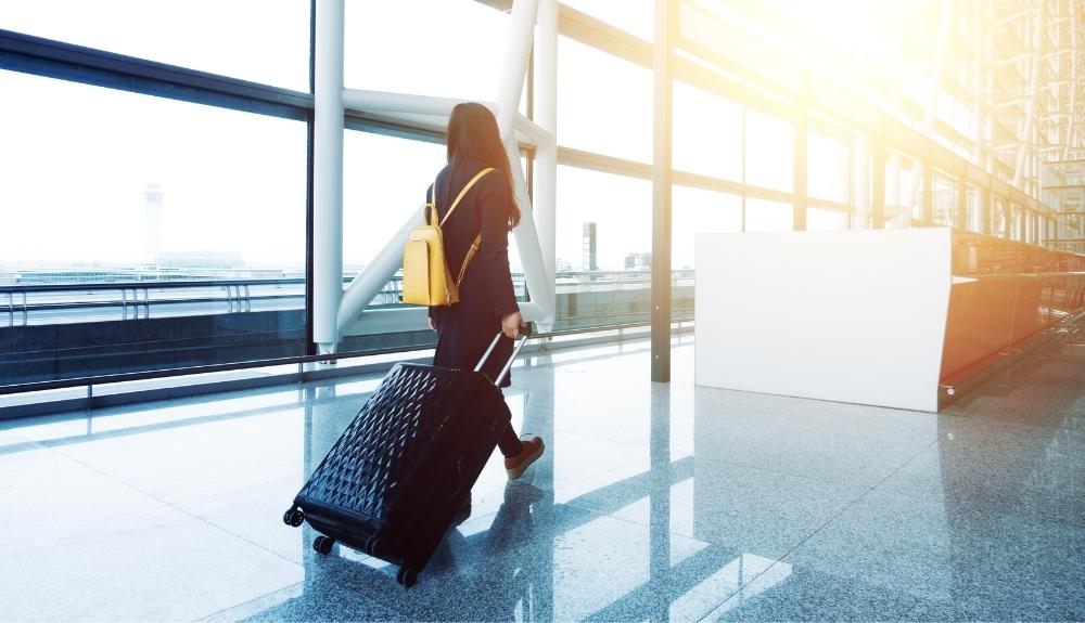 Woman dragging suitcase through airport terminal, emphasis on travel essentials for women.