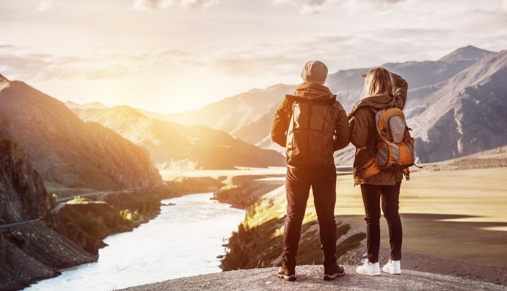 Couple in the foreground, mountains and lake in the background with a setting sun.