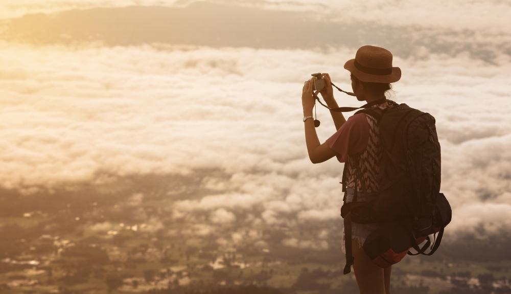 Woman taking a picture in the foreground, a low altitude city and cloud cover in the background. 