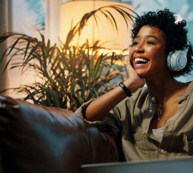 Woman with curly hair with headphones on listening to podcast joyfully.