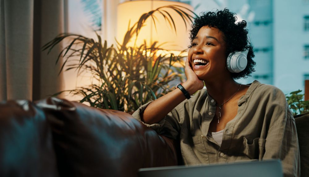Woman with curly hair with headphones on listening to podcast joyfully.